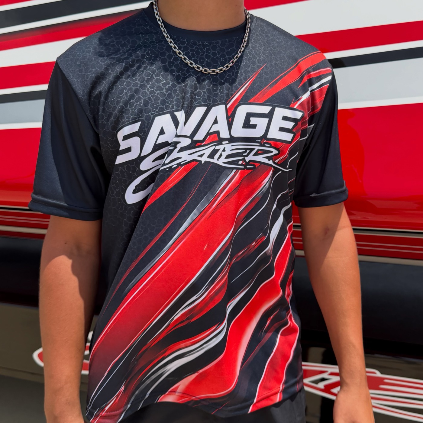Savage Skater race team t-shirt in black, red and white, worn beside a race boat